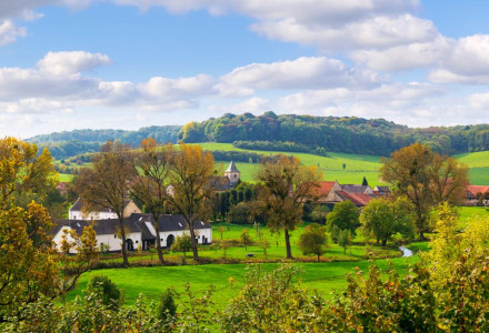 Paisaje rural con campos verdes y edificios cerca de Herkenbosch, Limburgo, Países Bajos bajo un cielo azul.