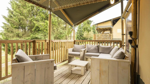 Terraza de madera con cómodos asientos en la tienda safari Comet de Petite Suisse, Bélgica, con vistas al bosque.