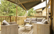 Terrasse en bois avec sièges confortables au tente safari Comet à Petite Suisse, Belgique, vue sur la forêt.