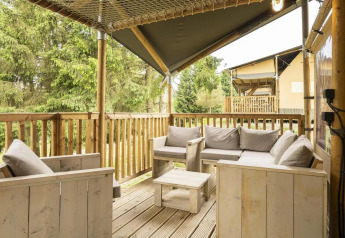 Terraza de madera con cómodos asientos en la tienda safari Comet de Petite Suisse, Bélgica, con vistas al bosque.