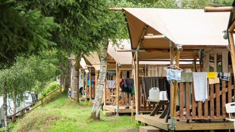 Række af safaritelte med træverandaer og ophængt tøj på Petite Suisse campingplads i Belgien.
