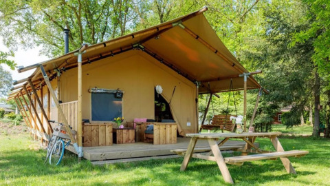 Safaritent Comet met houten terras, tuinbank, picknicktafel en fiets in een groene, rustige omgeving.