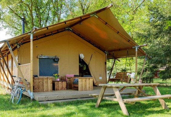 Safaritent Comet met houten terras, tuinbank, picknicktafel en fiets in een groene, rustige omgeving.