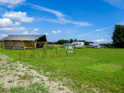 Safari-Zelt mit Toilette auf dem Boerderijcamping de Hinde in den Niederlanden mit grüner Wiese und Wohnwagen.