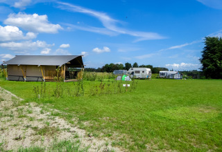 Safari-Zelt mit Toilette auf dem Boerderijcamping de Hinde in den Niederlanden mit grüner Wiese und Wohnwagen.