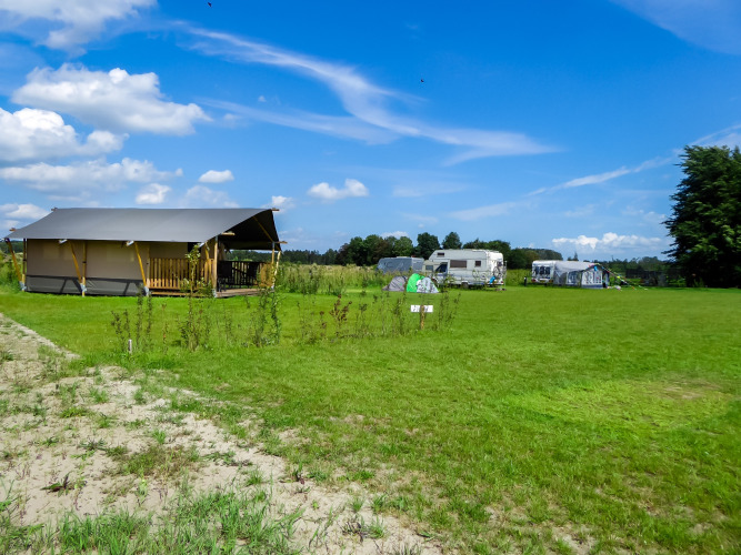 Safari tent with toilet at Boerderijcamping de Hinde in the Netherlands, surrounded by green fields and caravans.