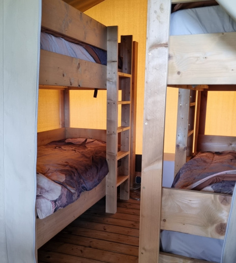 Interno di tenda safari con letti a castello in legno a Boerderijcamping de Hinde nei Paesi Bassi.