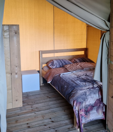 Interno di una tenda safari con letto matrimoniale e pavimento in legno presso Boerderijcamping de Hinde, Paesi Bassi.