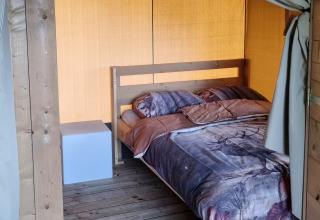 Interieur van een safaritent met dubbel bed en houten vloer bij Boerderijcamping de Hinde in Nederland.