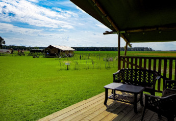 Uitzicht vanaf het terras van een safaritent op Boerderijcamping de Hinde in Nederland, met groene velden.