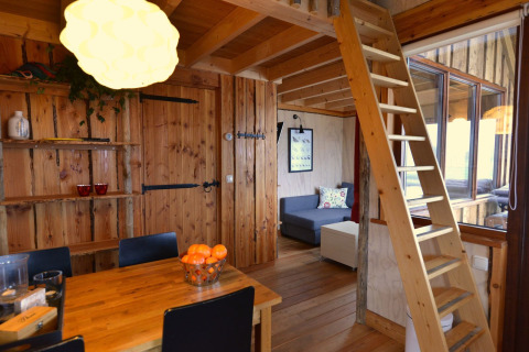 Interior acogedor de casa en el árbol con escalera, mesa de comedor y sofá en Camping de Koeksebelt, Países Bajos.