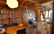 Cozy treehouse interior with wooden ladder, dining table, and sofa at Camping de Koeksebelt, Netherlands.