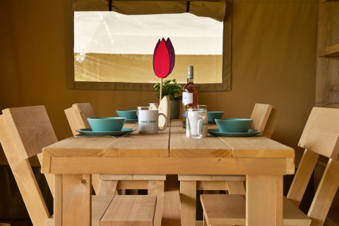 Dining table with blue dishware, wooden chairs, wine, and decor inside a safari tent at Camping Catsop.