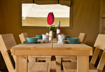 Mesa de comedor con platos azules, sillas de madera y vino en una tienda safari en Camping Catsop.