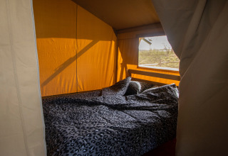 Interior view of a safari tent with double bed and blanket at Camping Catsop, Netherlands.