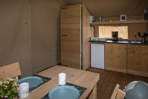 Interior of a safari tent at Camping Catsop, with wood furniture, kitchenette, dining table, and camp amenities.