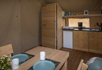 Interno di una tenda safari a Camping Catsop con mobili in legno, angolo cottura e tavolo da pranzo nei Paesi Bassi.