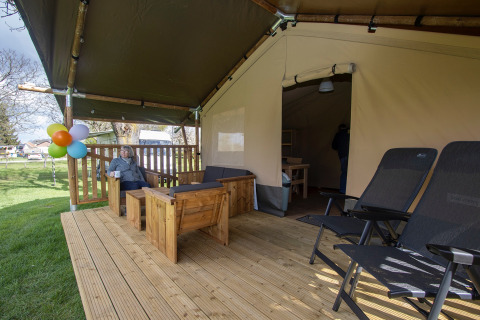 Terraza de madera de una tienda safari con zona de estar y tumbonas en Camping Catsop, Países Bajos.