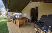 Terraza de madera de una tienda safari con zona de estar y tumbonas en Camping Catsop, Países Bajos.
