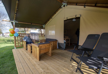 Wooden deck of a safari tent with seating area and loungers at Camping Catsop in the Netherlands.