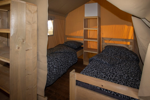 Innenraum eines Safarizeltes mit zwei Einzelbetten und Regalen, Tierprint-Bettwäsche bei Camping Catsop.