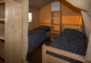 Inside a safari tent at Camping Catsop with two single beds, wooden furniture, and leopard print bedding.