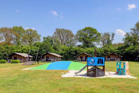 Parco giochi e bungalow al Camping Dal van de Mosbeek, parco vacanze a Overijssel, Paesi Bassi, circondato dal verde.
