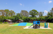 Legeplads og hytter på Camping Dal van de Mosbeek feriepark i Overijssel, Holland, omgivet af grønt.