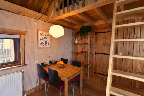 Vista interior de la casa en el árbol en Camping de Koeksebelt, Países Bajos, con mesa y escalera al altillo.