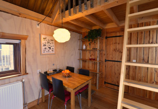 Binnenzicht van de boomhut op Camping de Koeksebelt in Nederland met eettafel en trap naar de slaapzolder.