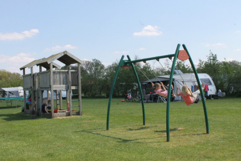 Kinder spielen an Schaukeln und einem Holzspielhaus auf dem Campingplatz Dal van de Mosbeek in Overijssel, Niederlande.