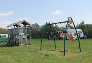 Kinderen spelen op schommels en in een houten speelhuis op camping Dal van de Mosbeek in Overijssel, Nederland.