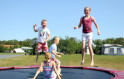 Børn leger og hopper på en trampolin på Camping Dal van de Mosbeek i Overijssel, Holland, på en solskinsdag.