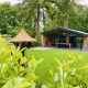 Udsigt over Family Lodge Deluxe ved De Thijmse Berg, Nederlandene, omgivet af grøn græsplane og skov.