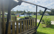 Blick von einem Safari-Zelt mit Terrasse auf Camping Dal van de Mosbeek, Wohnwagen und Spielplatz in den Niederlanden.
