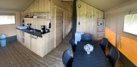 Indvendig udsigt over Safari telt med træ køkken, spisebord og stole på Camping Dal van de Mosbeek, Holland.