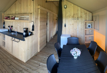Vista interior de una tienda safari con cocina de madera y mesa de comedor en Camping Dal van de Mosbeek, Países Bajos.