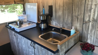 Área de cocina en tienda safari con estufa de gas, fregadero y cafetera en Camping Dal van de Mosbeek, Países Bajos.