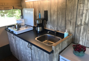 Área de cocina en tienda safari con estufa de gas, fregadero y cafetera en Camping Dal van de Mosbeek, Países Bajos.