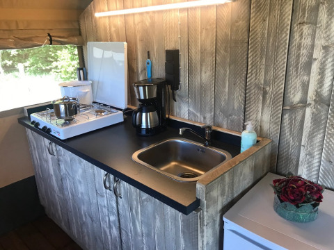 Compact safari tent kitchen area at Camping Dal van de Mosbeek with gas stove, sink, and coffee maker visible.