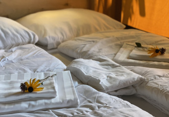 Cama hecha con sábanas blancas y girasoles en tienda safari en Camping Dal van de Mosbeek, Países Bajos.