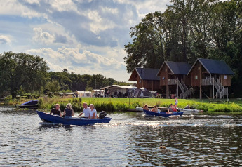 Folk sejler i både foran træhuse ved Camping de Koeksebelt i Holland på en solrig dag med blå himmel.