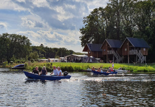 Mensen varen met een boot voor boomhutten aan Camping de Koeksebelt in Nederland op een zonnige dag.