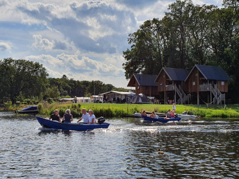 Personas navegando en bote frente a casas en los árboles en Camping de Koeksebelt, Países Bajos, día soleado.