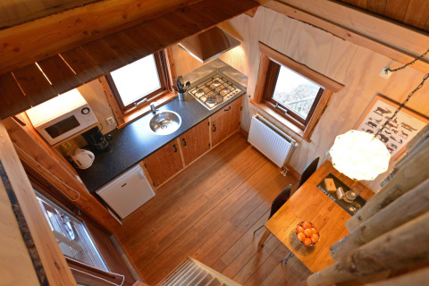 Vue en hauteur d’une cuisine de cabane dans les arbres avec sol en bois, table et fenêtres, Camping de Koeksebelt.