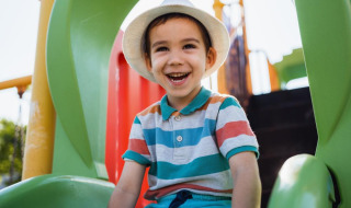 Garçon souriant avec un chapeau blanc sur un toboggan vert dans un parc de vacances avec hébergements glamping.