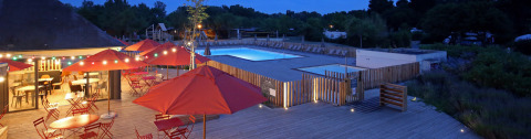 Evening view of Camping d'Angers - Lac de Maine with illuminated pool and terrace featuring red umbrellas.