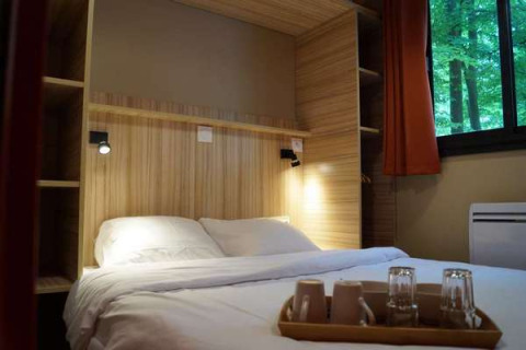 Schlafzimmer im Chalet Evasion, Camping d'Angers - Lac de Maine, mit Doppelbett und Waldblick.