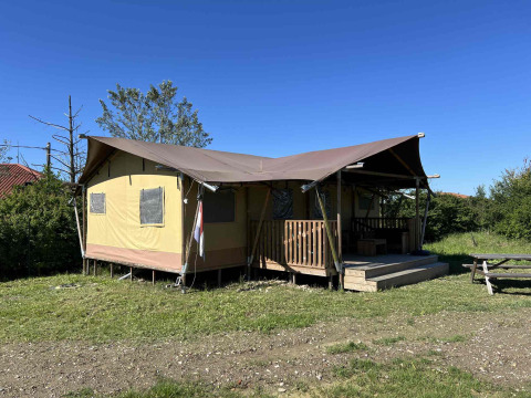 Safari Glamping telt med veranda under klar blå himmel, beliggende på græsplæne med picnicbord.