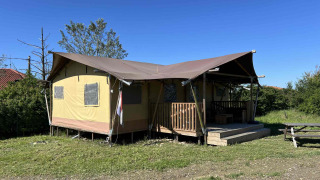 Tente de glamping safari avec terrasse couverte sur pelouse, sous ciel bleu, et table de pique-nique.